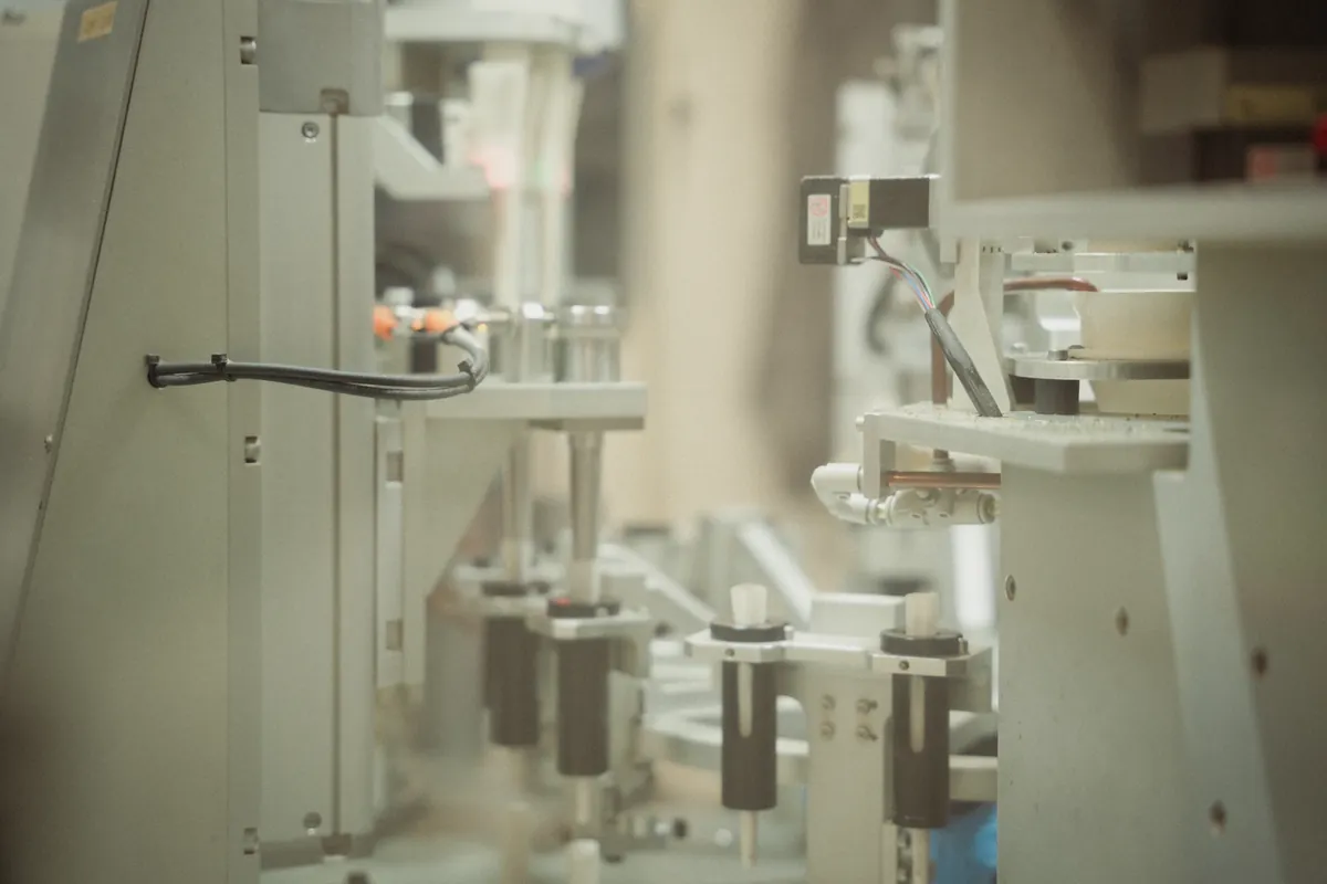 Close-up of production machinery with metal brackets, rods, cylinders, and wires.